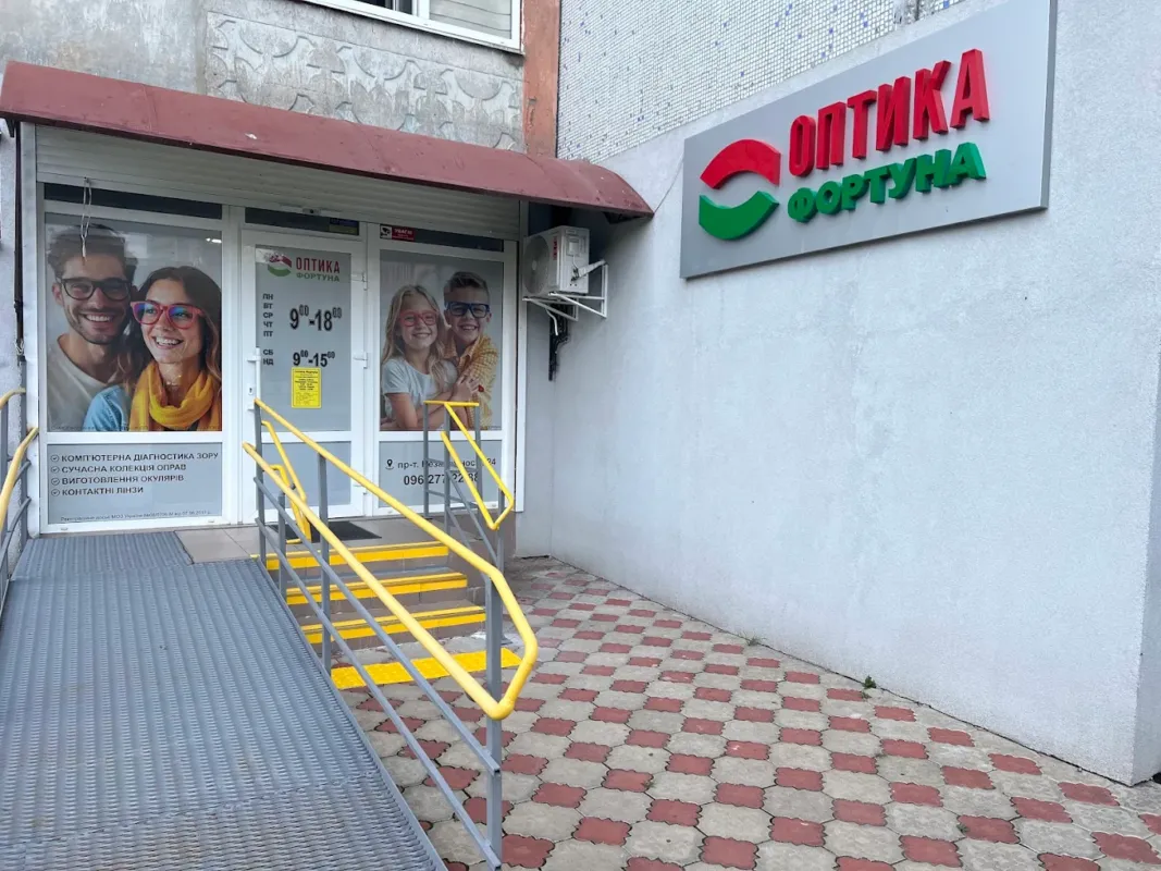 Вхід до Оптики Фортуна в Нетішині, просп. Незалежності, 24: вивіска, пандус і сходи з поручнями